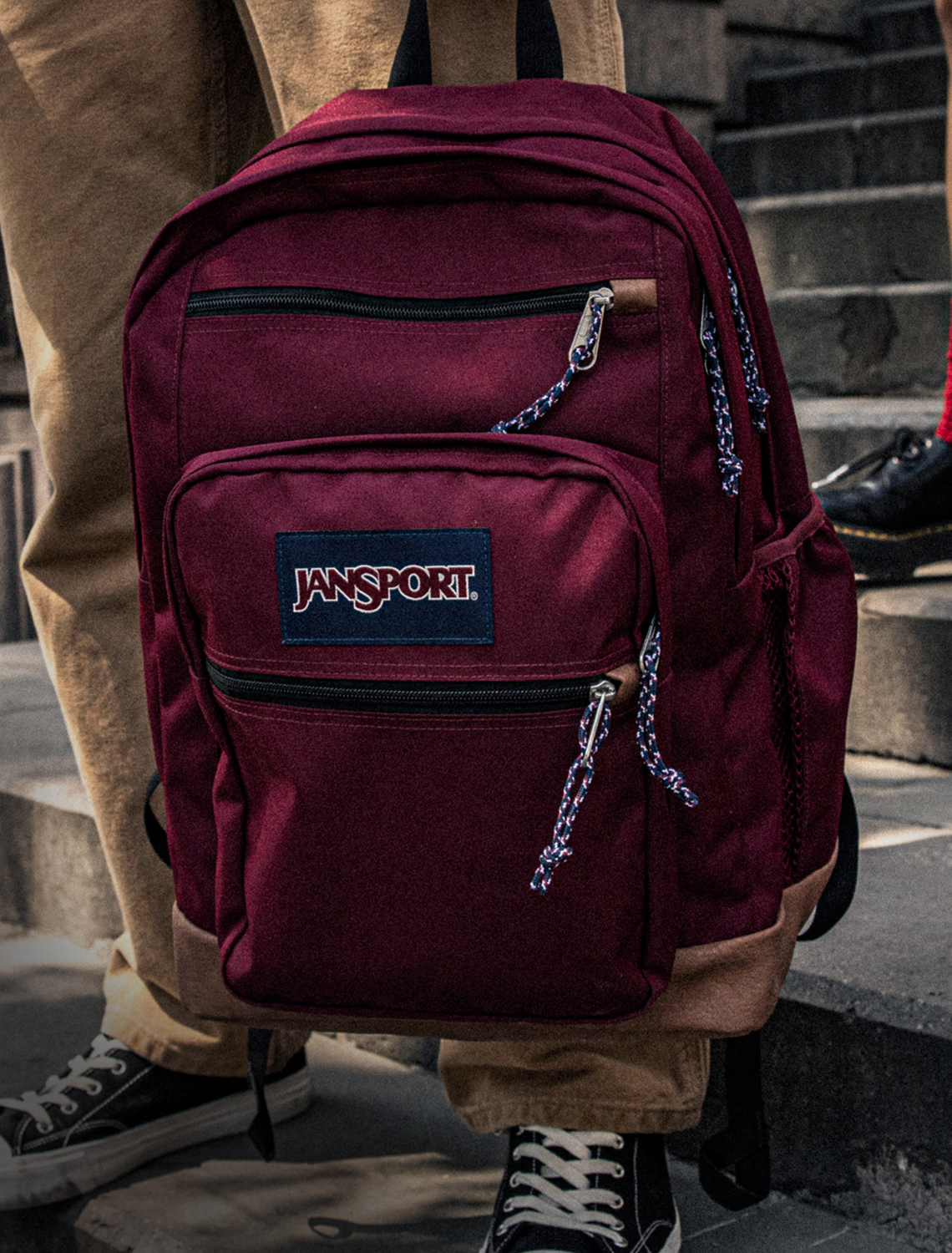 Maroon Jansport backpack worn by a person on stone steps.