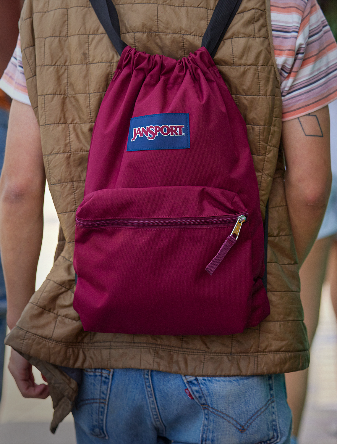Person wearing a maroon drawstring bag with a Jansport logo on a blurred background
