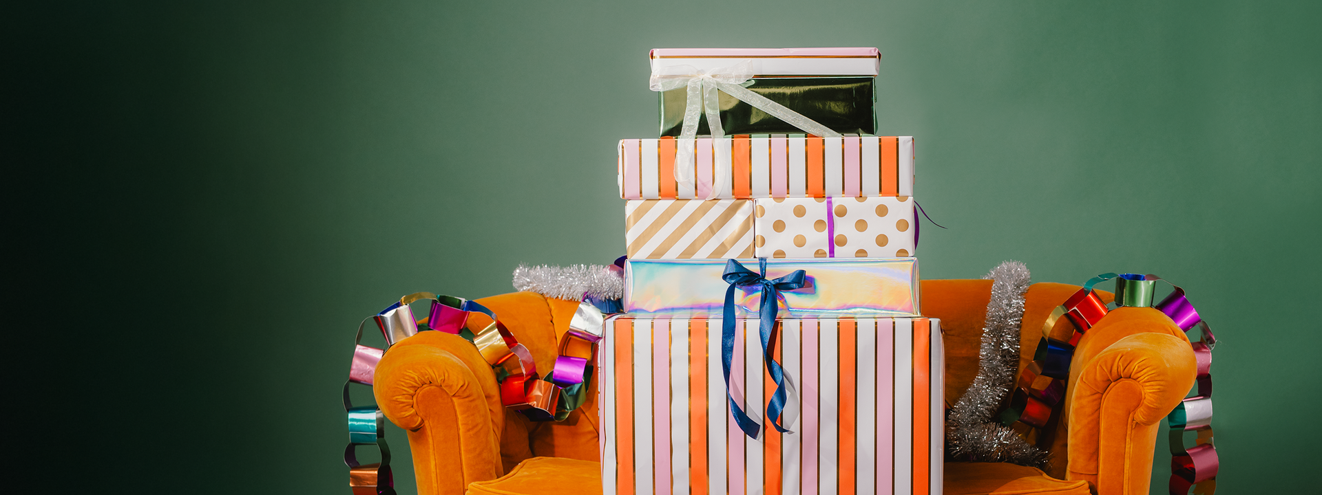 Stack of colorful gift boxes on a chair with a green chalkboard background