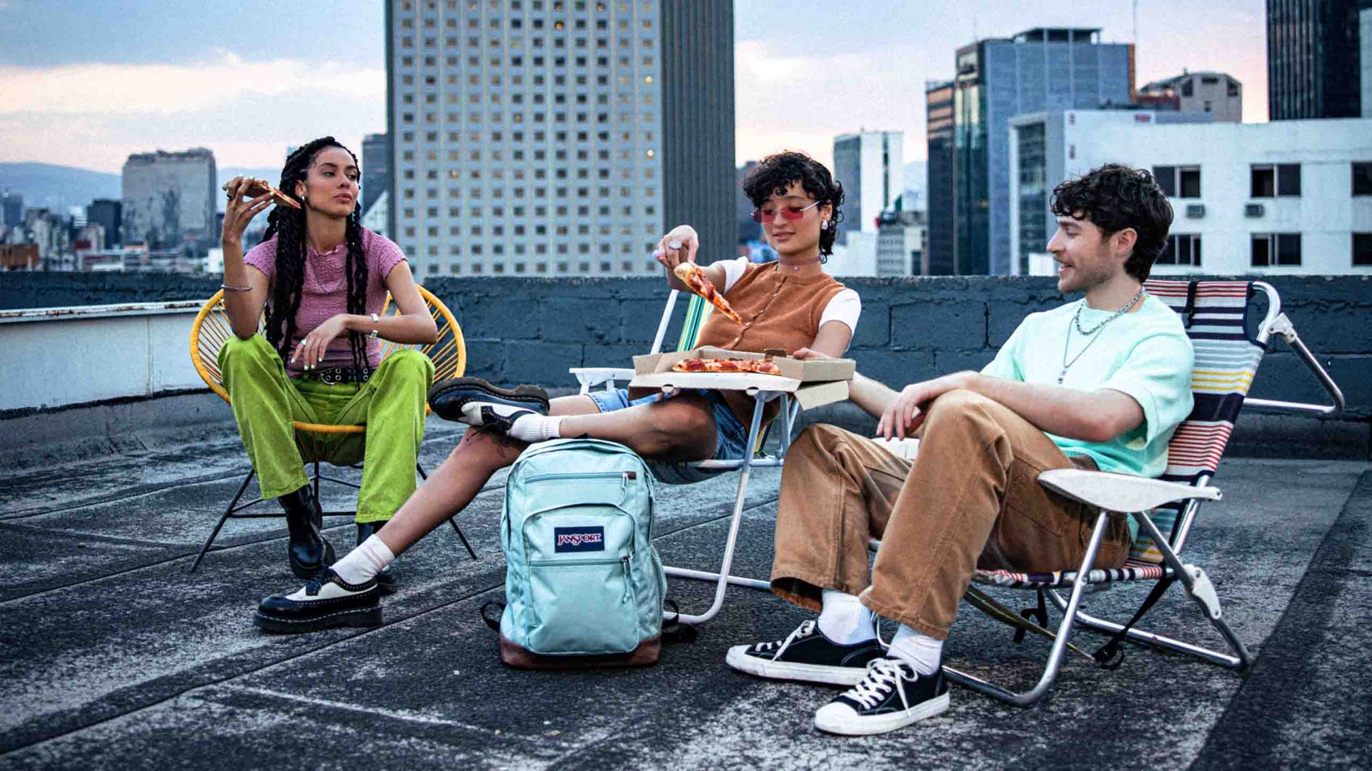 Older teens sitting on a roof top, eating pizza with their JanSport Backpacks