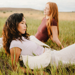 A girl in a field in soft neutral tones wearing a JanSport Unphased cross body bag in moonflower