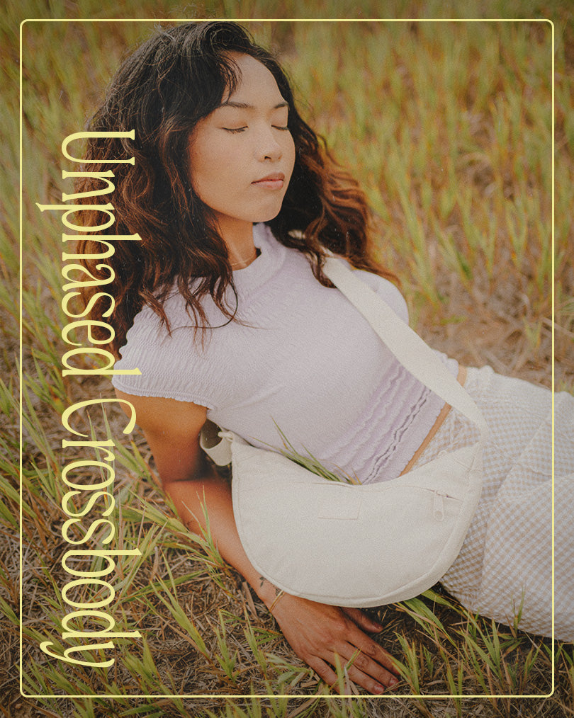 Woman sitting in a field wearing a white JanSport Waistpack with 'Unphased Crossbody' text overlay
